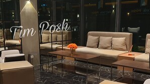 En modern hotellobby med en soffa, fåtöljer, ett soffbord och en vas med blommor.