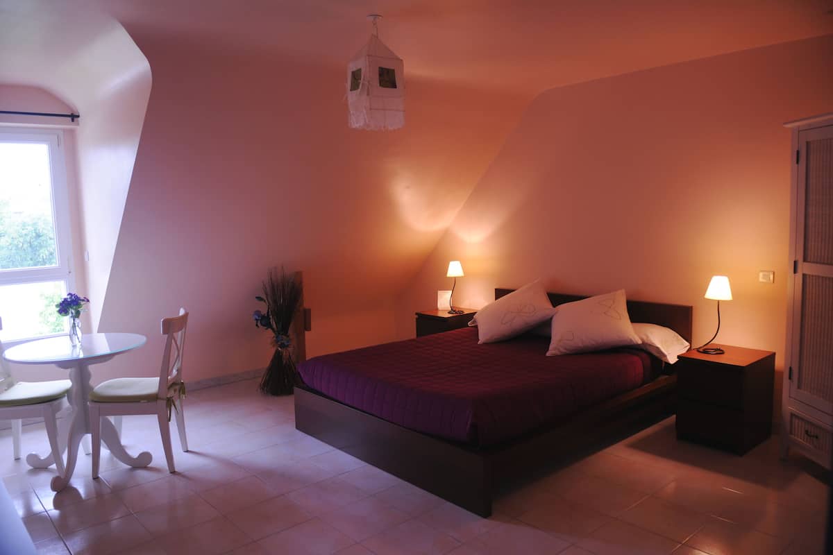 A bedroom with a bed, bedside tables, a nightstand, a chair, a small round table, and a window.