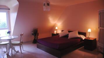 Une chambre à coucher comprenant un lit, des tables de chevet, une commode, une chaise, une petite table ronde et une fenêtre.