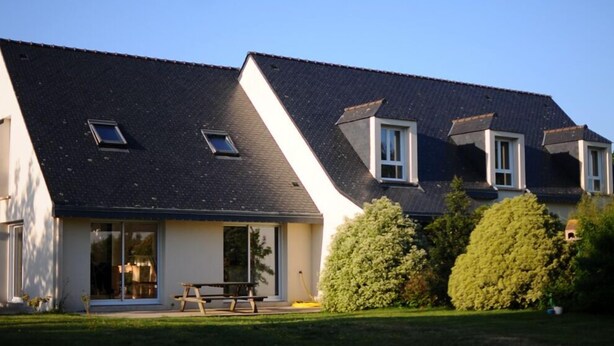 Une maison à deux étages, dotée d’un toit en pente, de grandes fenêtres et d’un espace patio.
