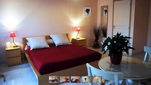 Une chambre à coucher avec un lit, des tables de chevet, une table ronde avec des chaises, une plante en pot et une porte.