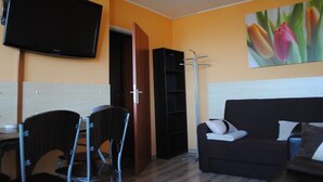 Quarto com sofá, cadeiras, televisão, quadro de tulipas e uma porta.