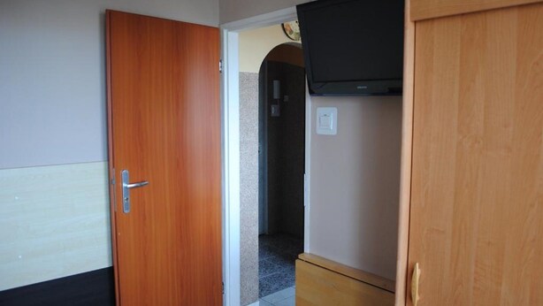 Quarto com porta de madeira, televisão fixada na parede e um armário de madeira.