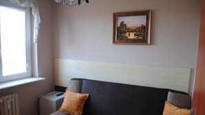 Quarto com sofá de cor escura, duas almofadas, um radiador, uma mesinha e um quadro na parede.