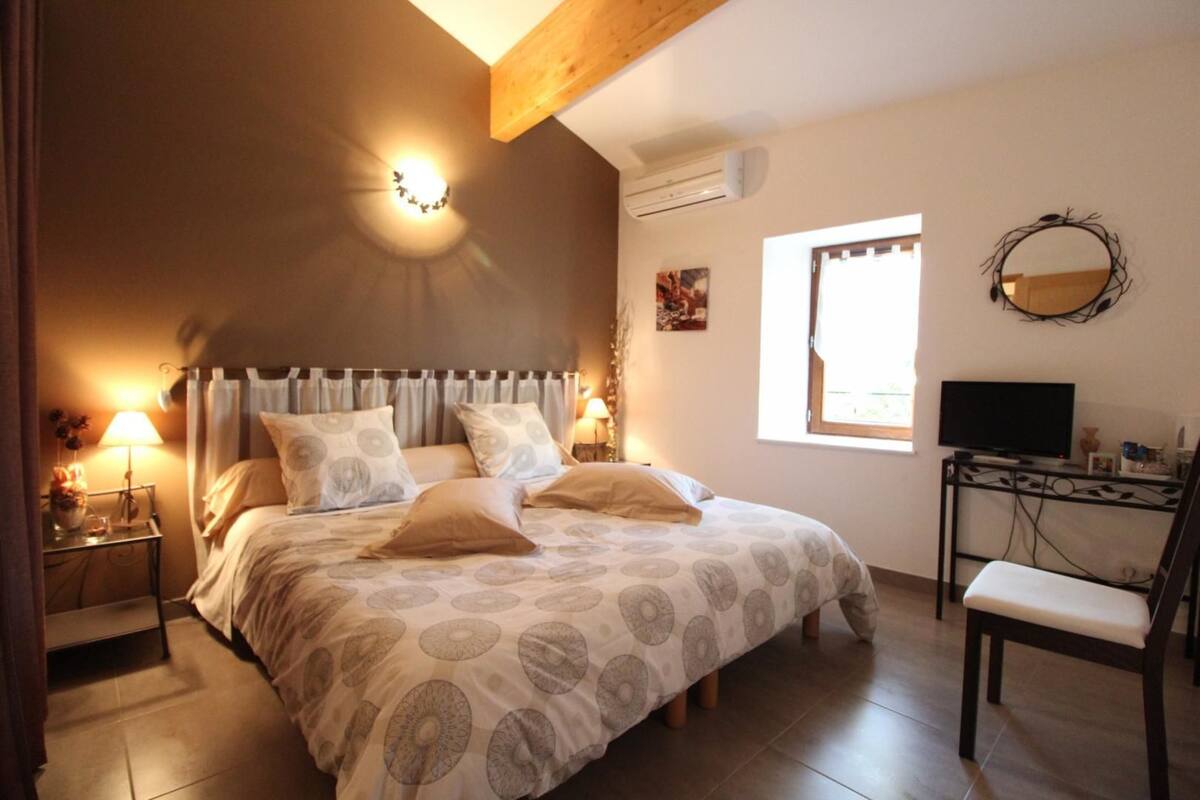 A bedroom with a bed, bedside lamps, a TV, a desk, and a window.