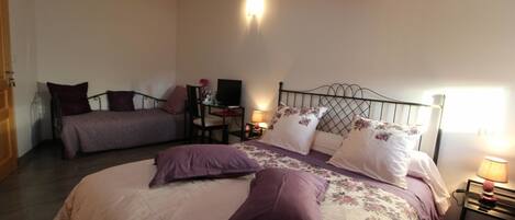 A bedroom with two beds, a desk with a chair, a TV, and a lamp.
