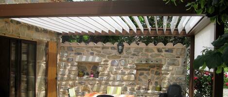 Eine Steinsäule mit eingebautem Kamin, Sitzbereich im Freien mit Stühlen und Tisch, und eine Pergola darüber.