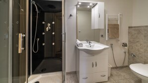 Ein modernes Badezimmer mit einer gläsernen Duschkabine, einem weißen Waschbecken mit Spiegel darüber und einer Toilette.