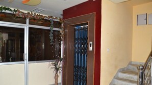 Vestíbulo de hotel con puerta de vidrio, escalera y una planta en maceta.