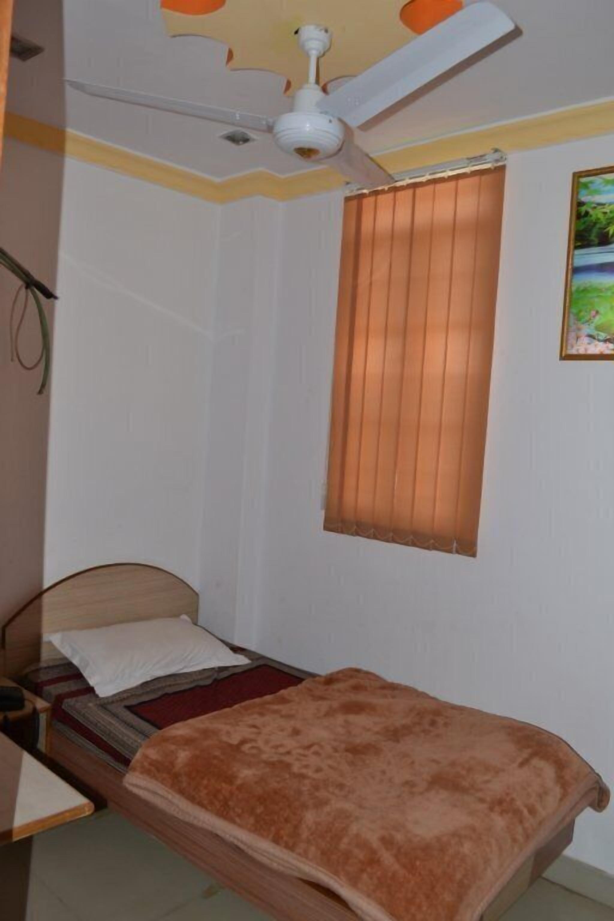 A bedroom with a bed, a ceiling fan, a window with blinds, and a painting on the wall.