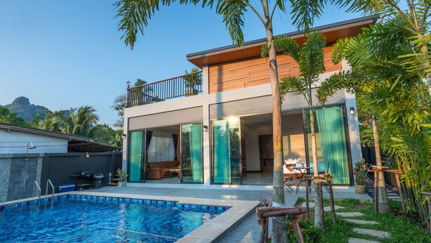 Ein modernes, zweistöckiges Haus mit Swimmingpool, großen Glaswänden und einem Balkon.