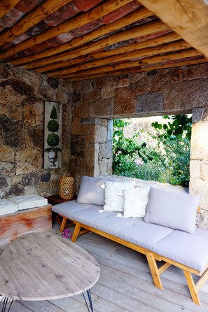 Une pièce aux murs de pierre, avec un plafond en bois, un banc rembourré et une table ronde en bois.