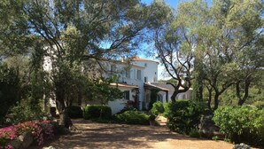 Un bâtiment blanc, doté d’un toit recouvert de tuiles, entouré d’arbres et d’arbustes.