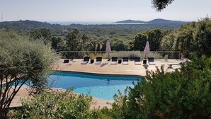 Un espace aménagé au bord de la piscine, avec des chaises longues et des parasols, entouré de verdure et offrant une vue sur un paysage pittoresque.