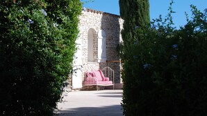 Un bâtiment en pierre, avec un arbre grand et étroit qui se dresse devant, le tout entouré de verdure.