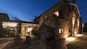 A stone building with a well-lit entrance and outdoor seating area. - Beautiful restored farmhouse with swimming pool in the quiet of the Sienese hills. (Trequanda)