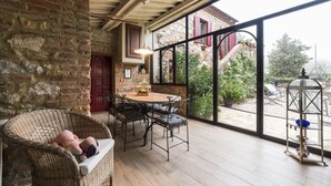 A cozy patio area with wicker furniture, a round table, and a view of a garden through large windows. - Beautiful restored farmhouse with swimming pool in the quiet of the Sienese hills. (Trequanda)