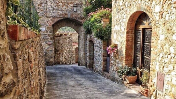 A narrow stone pathway leading through an old stone building with arched doorways and potted plants. - Beautiful restored farmhouse with swimming pool in the quiet of the Sienese hills. (Trequanda)