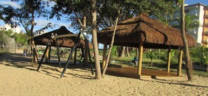 Une plage avec un pavillon à toit de chaume et une balançoire.