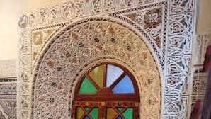 A room with a decorative arched window, intricate wall patterns, and a patterned floor. - Riad Bab Berdaine (Meknes)