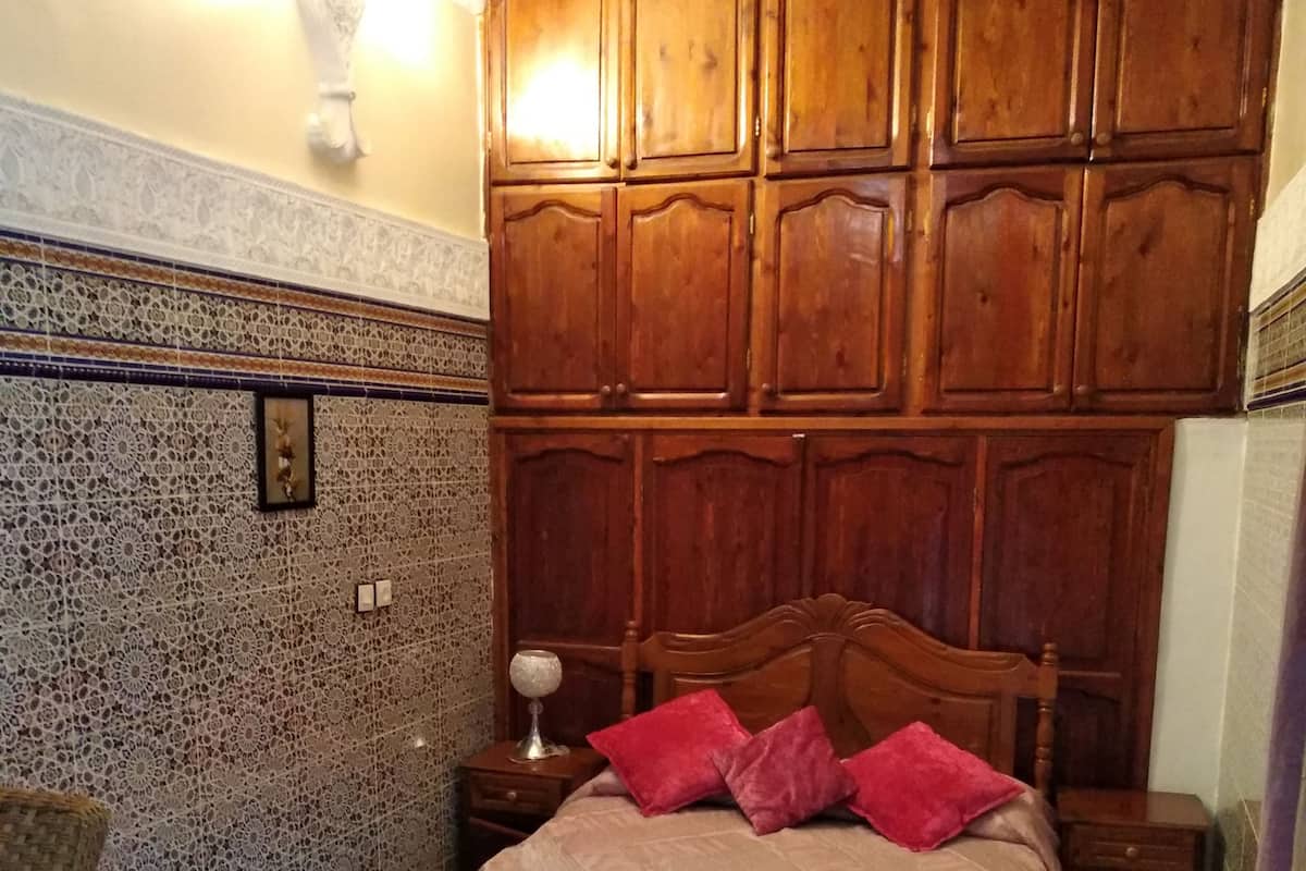 A bedroom with a wooden headboard, a patterned rug, and a nightstand with a lamp.