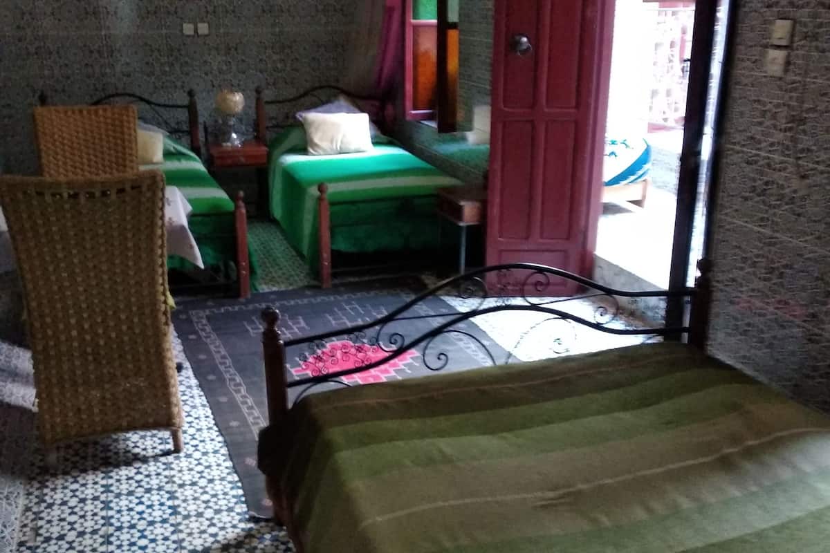 A room with a bed, a chair, a small table with a lamp, and a window with a view of the outside.