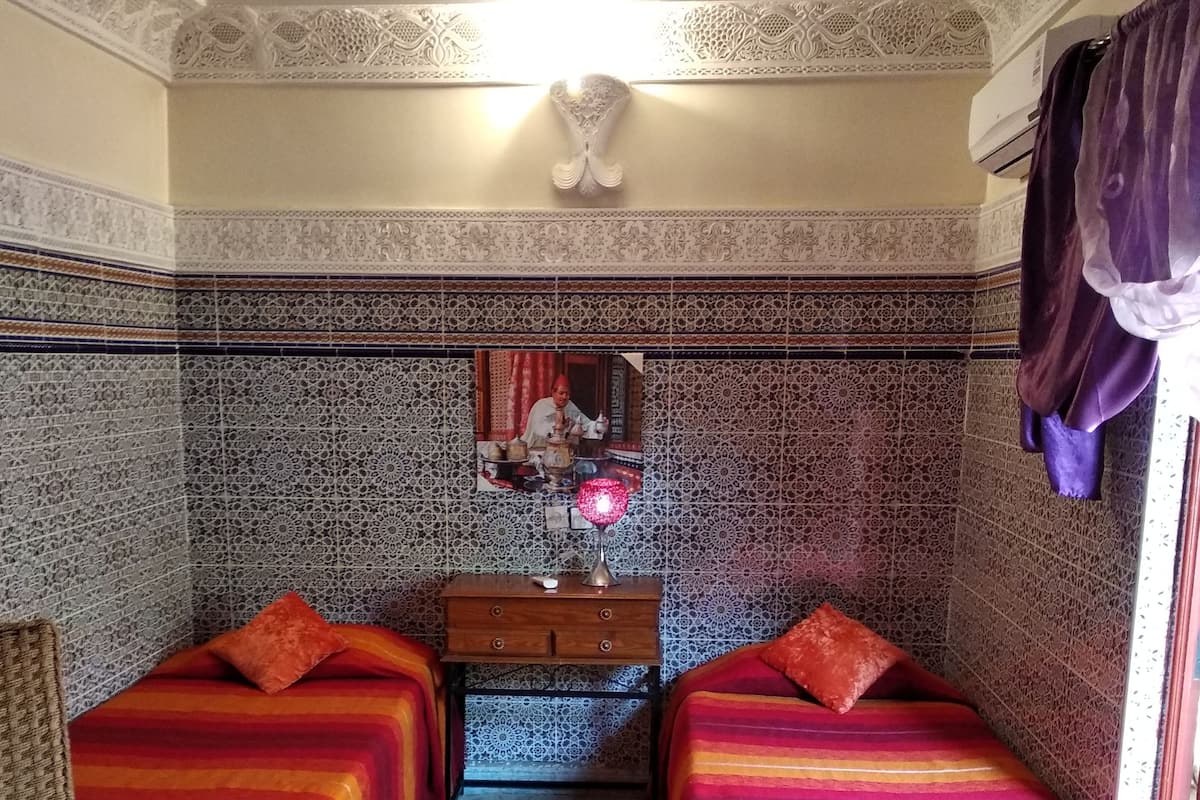 A room with two beds, a wooden nightstand, a patterned rug, and a decorative mirror.