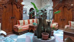 A traditional interior with ornate wooden furniture, patterned walls, and a central seating area with cushions and potted plants. - Riad Bab Berdaine (Meknes)