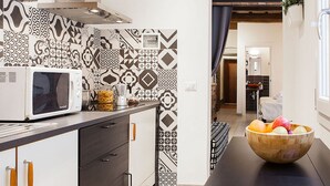 A modern kitchen with patterned backsplash, a microwave, and a wooden bowl with fruit on the counter. - Santa Croce Apartment (Florence)