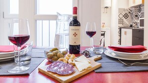 A dining table with a bottle of Chianti wine, glasses, olives, cheese, and cured meats. - Santa Croce Apartment (Florence)