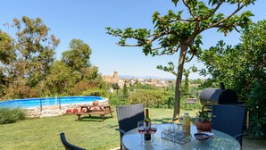 Une terrasse avec une table ronde en verre, des sièges d’extérieur, un barbecue et une piscine.