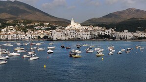 Une ville côtière aux bâtiments blancs, avec une église imposante et de nombreux bateaux dans le port.