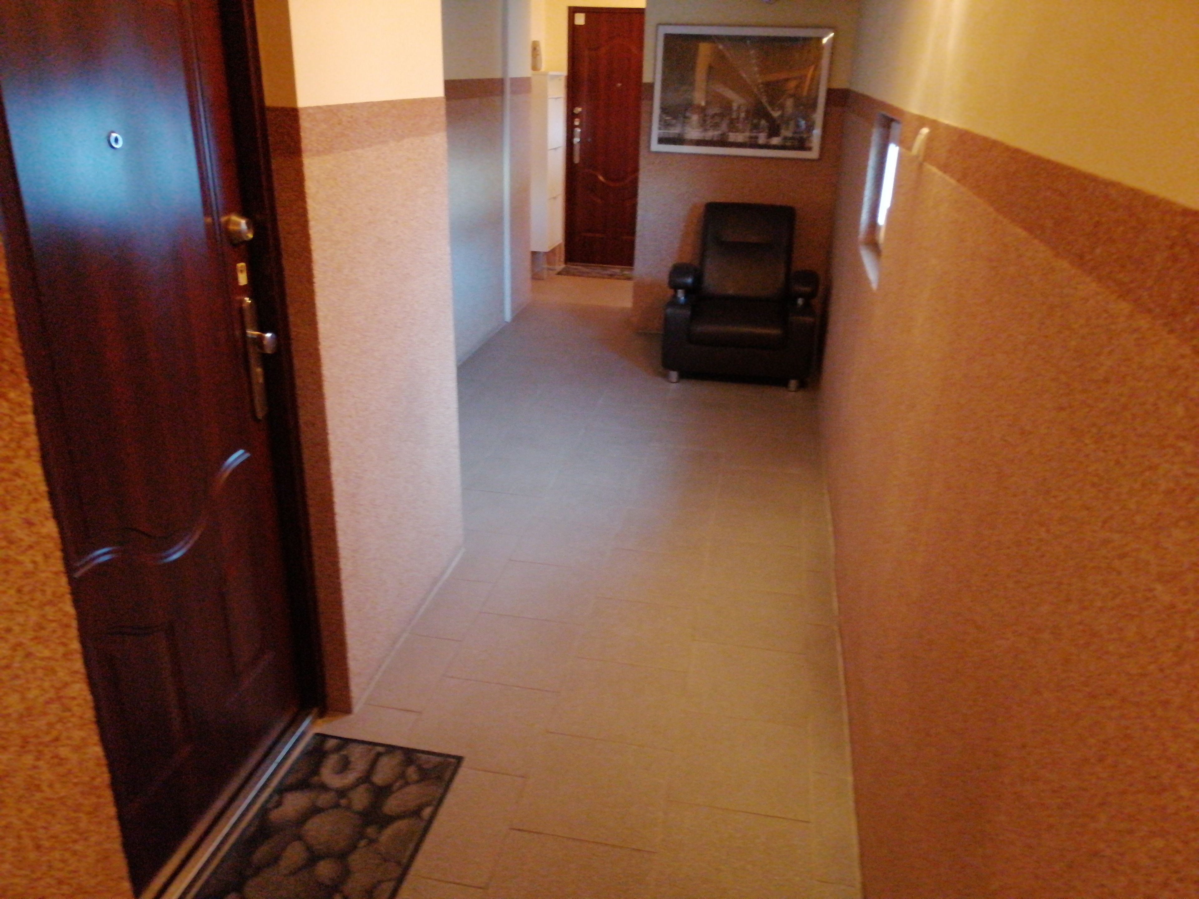 Un pasillo con una puerta de madera, una silla negra y un cuadro en la pared.