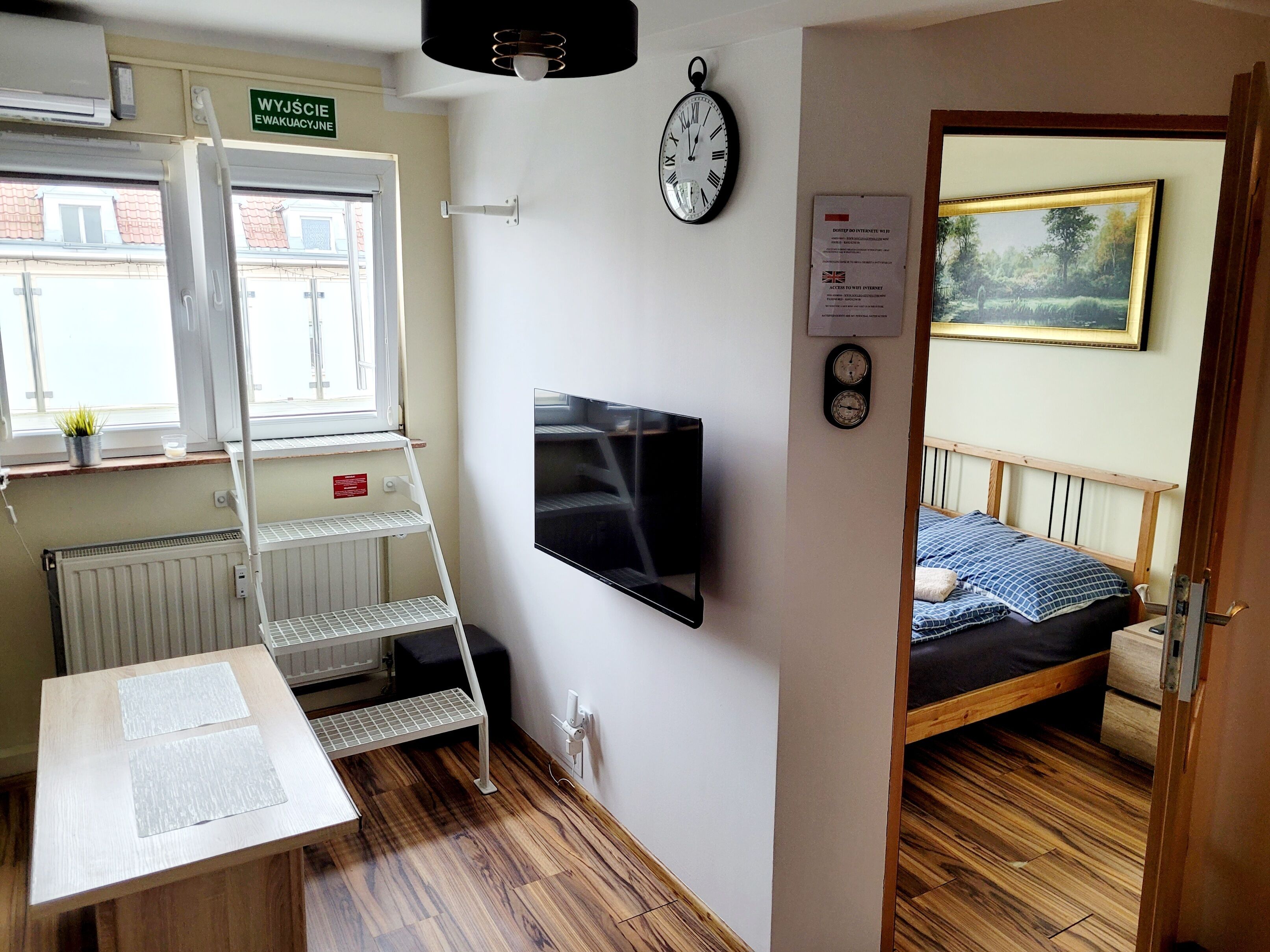 A small room with a bed, a TV, a clock, and a ladder.