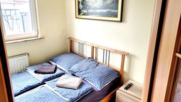 A small, single-bed room with a wooden headboard, a bedside table, and a framed picture on the wall.