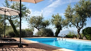 A swimming pool with lounge chairs and umbrellas, surrounded by trees and a stone wall. - Relais La Torricella - Villa in the Sorrento Peninsula (Vico Equense)