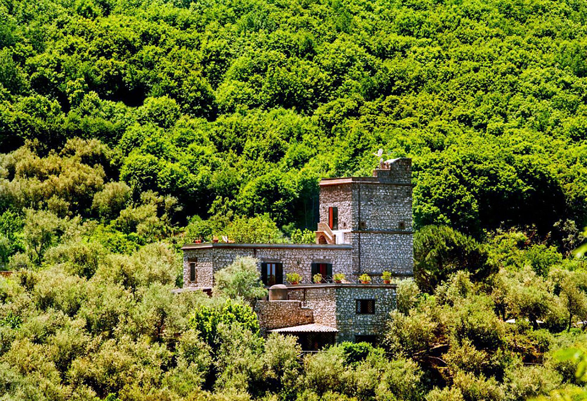 Un bâtiment en pierre à plusieurs étages, entouré d’une forêt verdoyante et dense.