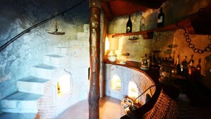 A rustic room with stone walls, a wooden ceiling, and a brick fireplace. There are shelves with bottles and a hanging light fixture. - Relais La Torricella - Villa in the Sorrento Peninsula (Vico Equense)