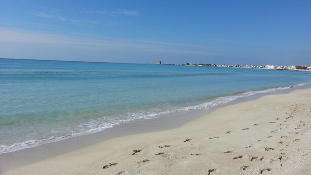 A beach with clear blue water, sandy shore, and buildings in the distance. - Holiday House '' Lu Barocco '' (San Pancrazio Salentino)