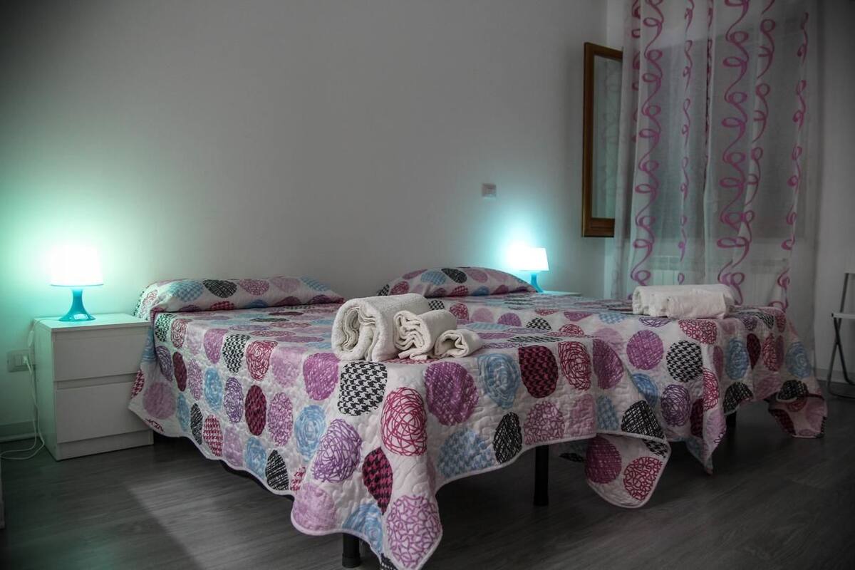 A double bed with a patterned quilt, two bedside lamps, and a folded towel on the bed.