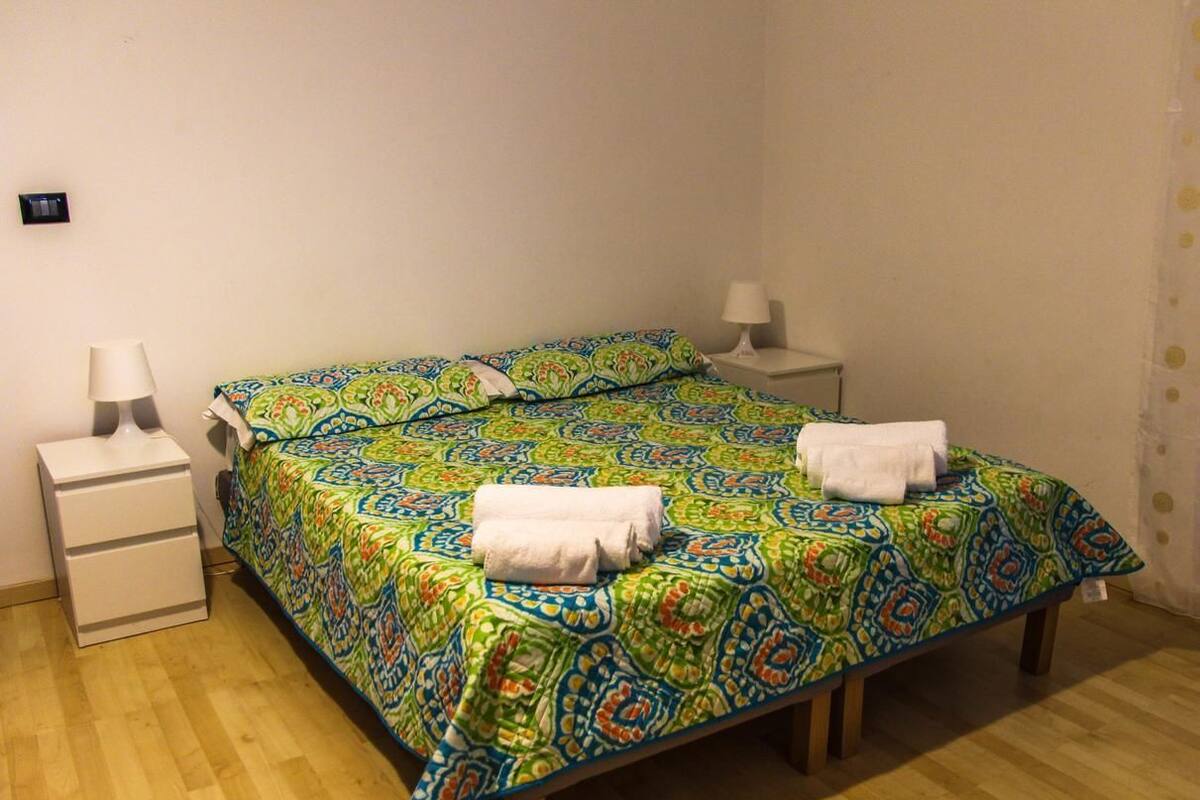 A single bed with a colorful patterned bedspread and two white bedside tables with lamps.