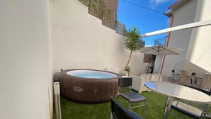 A backyard with artificial grass, a hot tub, a table, and chairs.