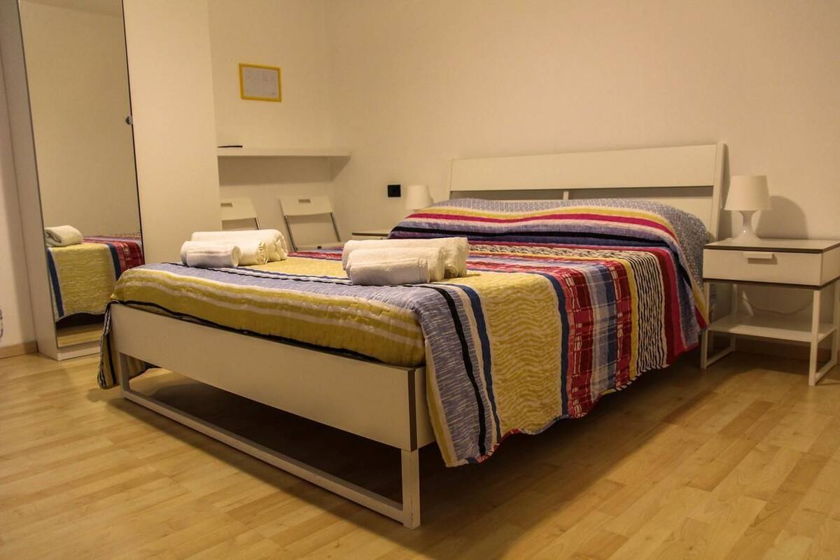 A neatly made bed with striped bedding, a bedside table with a lamp, and a mirror on the wall.