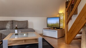 A modern living room with a sofa, a coffee table, a TV, and a wooden staircase.