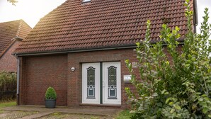A brick house with a tiled roof, a small garden, and a potted plant in the front yard.