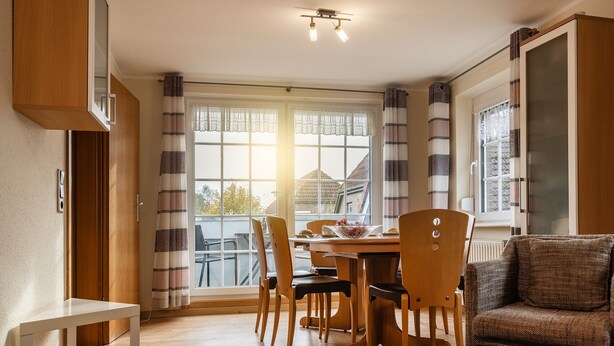 A dining area with a wooden table and chairs, a sofa, and a window with curtains.