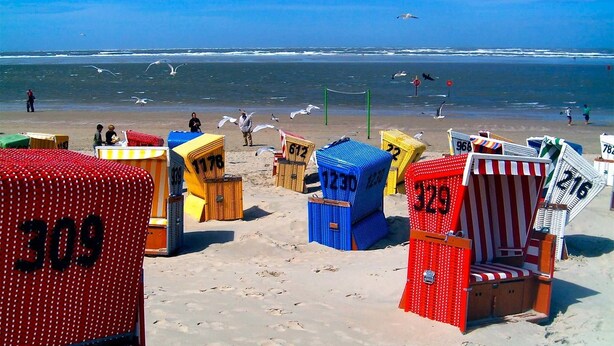 Beach huts numbered 309, 178, 1230, 329, and 216 on a sandy beach with the ocean in the background. - Gästehaus, Das Fischerhus (Esens)