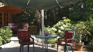 An outdoor patio with two tables and four chairs, surrounded by greenery and a wooden fence. - Gästehaus, Das Fischerhus (Esens)