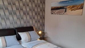 A modern bedroom with a bed, a headboard with a geometric pattern, a bedside table with a lamp, and a framed picture on the wall. - Gästehaus, Das Fischerhus (Esens)