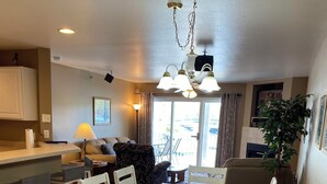 Un coin repas avec une table et des chaises en bois, un coin cuisine avec des placards et un plan de travail, et un salon avec un canapé et une lampe.